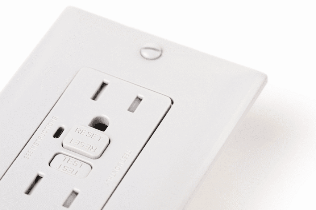 Close-up view of a white GFCI outlet with visible test and reset buttons, showing proper GFCI outlet installation.
