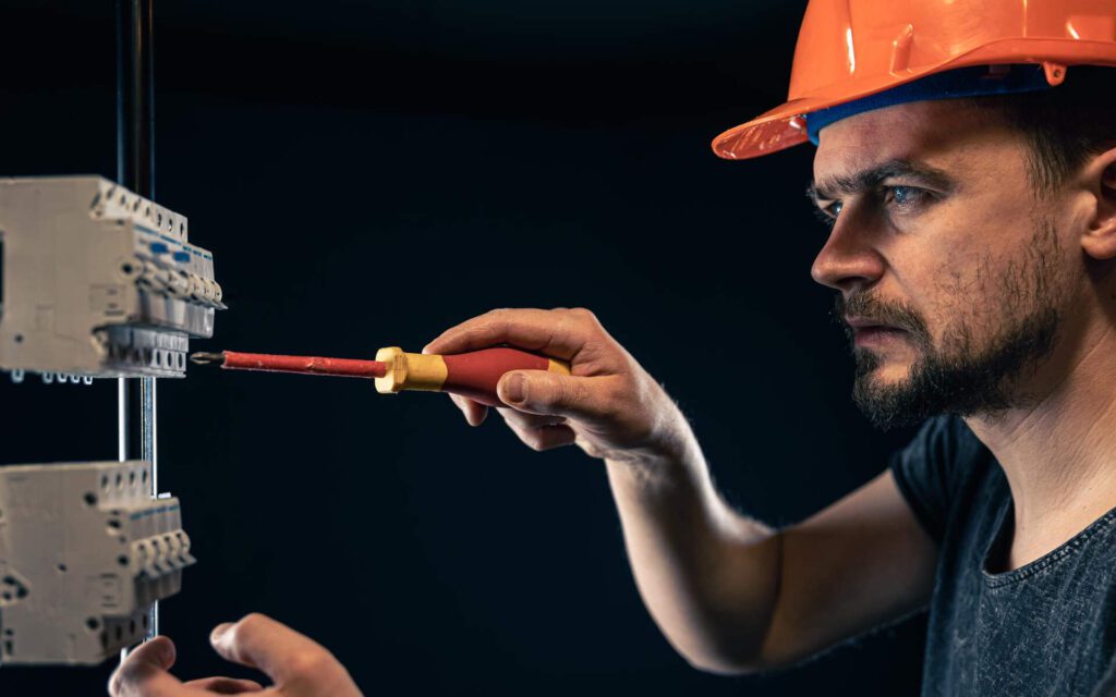 Certified electrician using an insulated screwdriver to adjust components on an electrical panel.