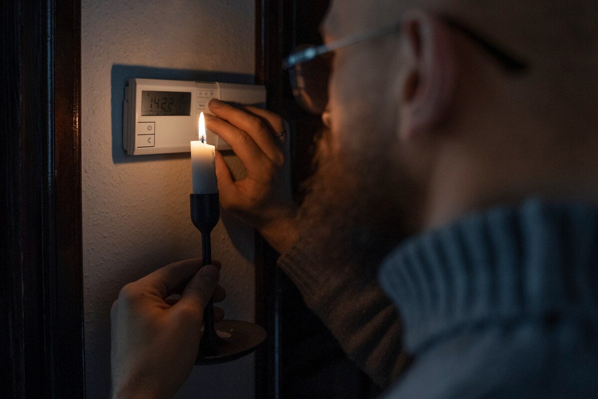 Man checking thermostat by candlelight during a power outage, highlighting the need for surge protector installation.