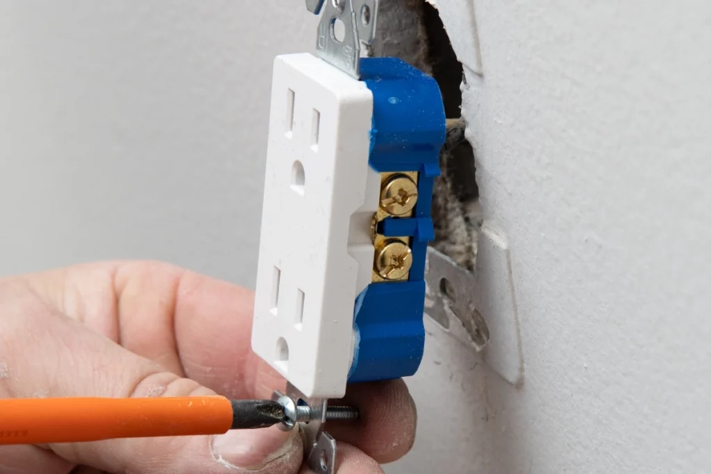 An electrician installs a wall outlet with visible brass terminals using a screwdriver, part of work on GFCI outlets in Lake Highlands.